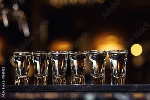 Alcoholic shots of tequila or strong drink in small glasses,Barman at work,Barman pouring hard spirit into glasses in detail, with lime garnish ready to be served,concept about service and beverages