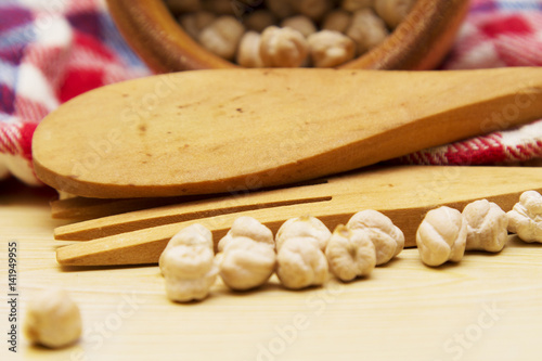Wooden bowl with chickpeas and spoon on wooden table with red tablecloth