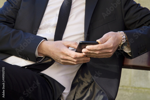 Young man in suit sitting in park using mobile phone