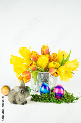 Dekoration für Ostern mit bunt gestreiften Ostereiern, einem kleinen Osterhasen und einem Strauß rot gelbe Tulpen, weißer Hintergrund mit Textfreiraum, vertikal