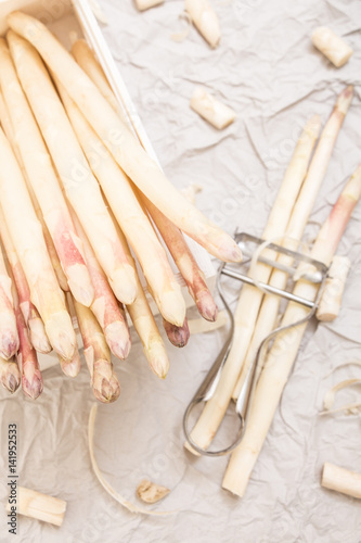 Bunch of white asparagus in box, on crumpled paper with metallic peeler.