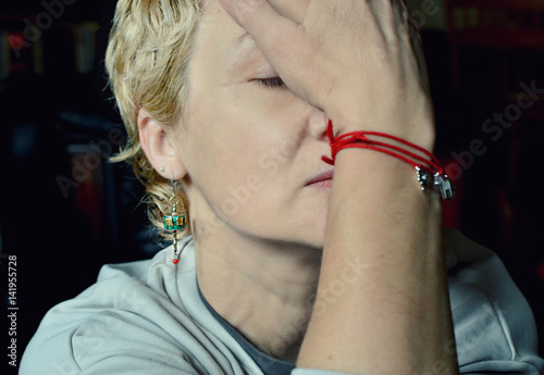 Portrait of a blond short haired woman covering her face with her hand