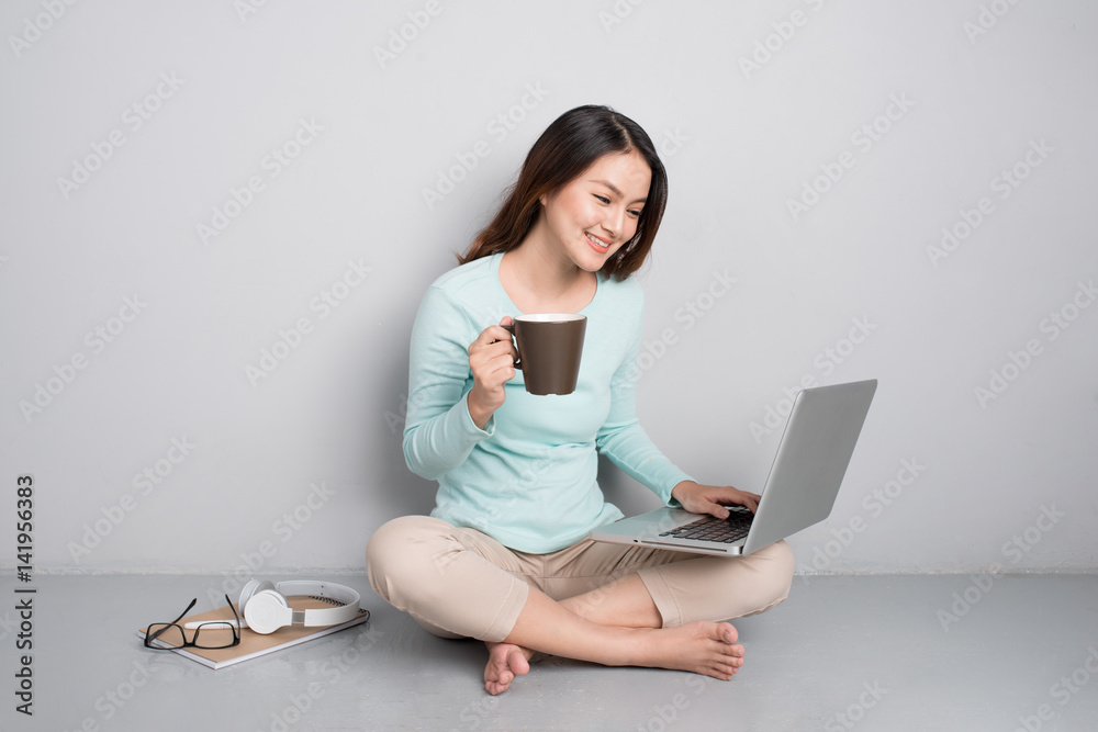 Fototapeta premium Happy casual beautiful asian woman working on a laptop sitting on floor at home.
