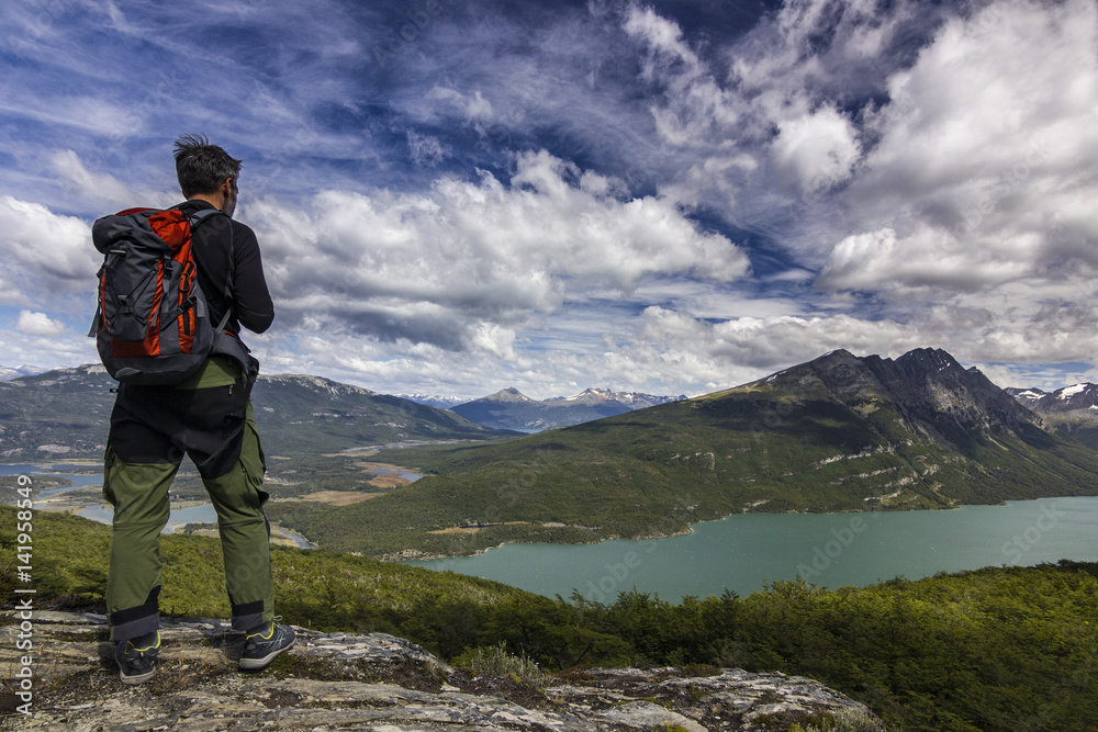 man with backpack standing on the cliff in mountains at above lake