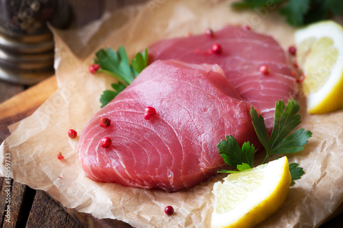 Fresh raw tuna steaks on parchment paper with pink pepper corns, parsley and slices of lemon
