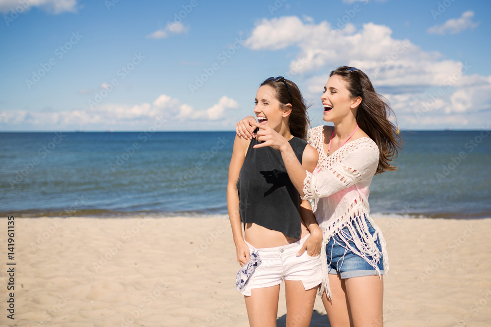 Two pretty girls on beach looking at something laughing