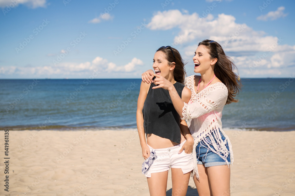 Two pretty girls on beach looking at something laughing Two pretty girls on beach looking at something laughing