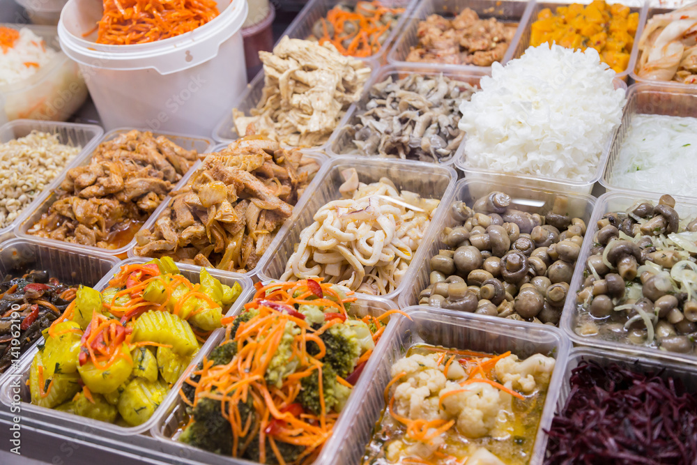 Korean snacks and salads on display in trays on the market.