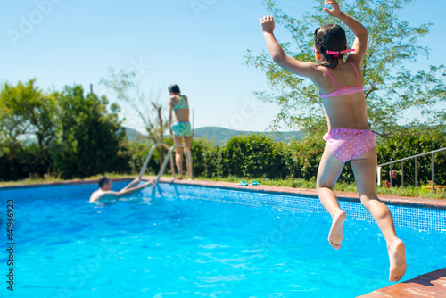 Happy little active girl jumping into outdoor swimming pool during family summer vacation. Kids learning to swim. Water fun for children. Kids sport and holiday.