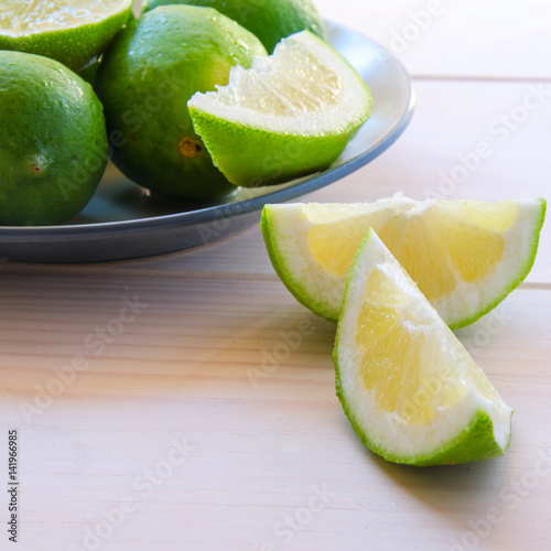 Fresh organic limes with slices in ceramic plate on wooden table. Limefruit background with copy space. photo