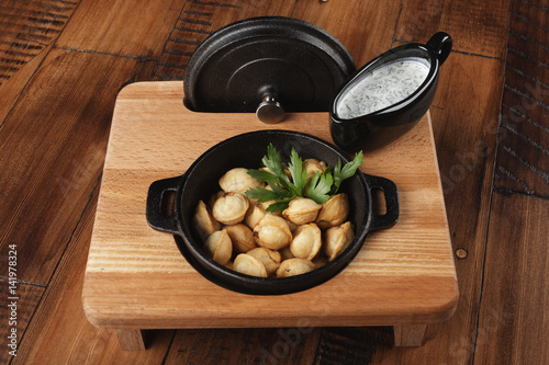 Cooked meat dumplings (pelmeni, chuchpara) in black pan with sauce. wooden background. photo