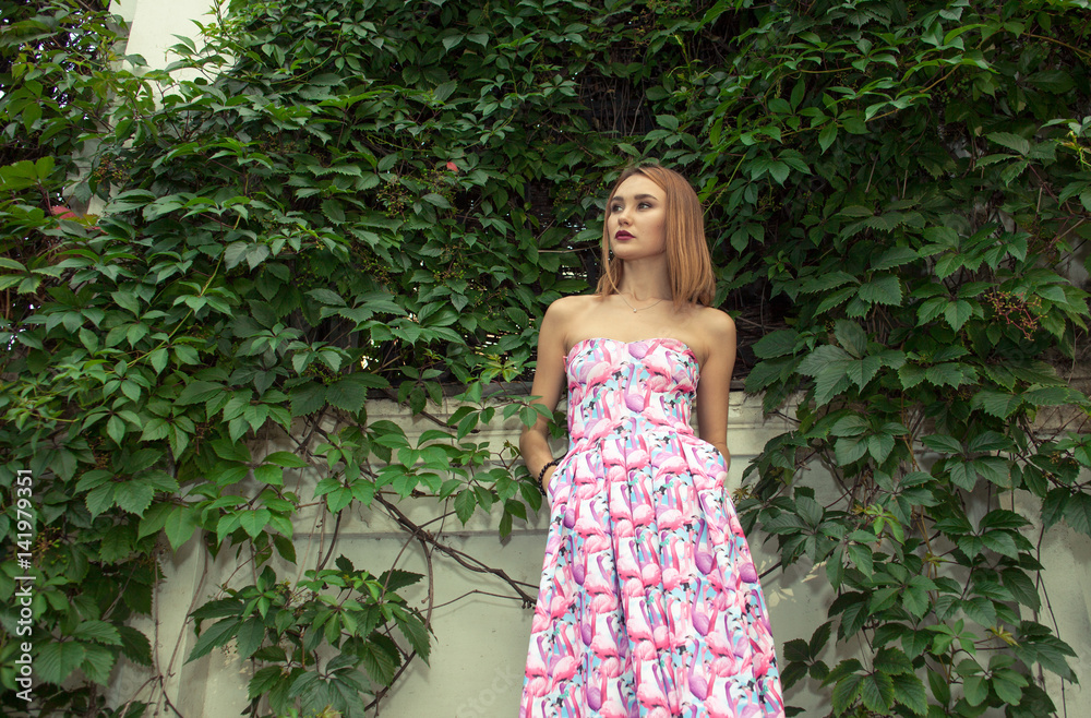 young attractive mixed race girl in pink dress outdoor near wall with ivy looks left young attractive mixed race girl in pink dress outdoor near wall with ivy looks left