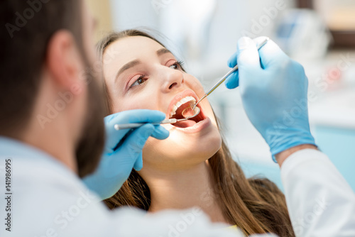 Dentist examining patient teeth with a mouth mirror and dental excavator. Close-up view on the woman's face
