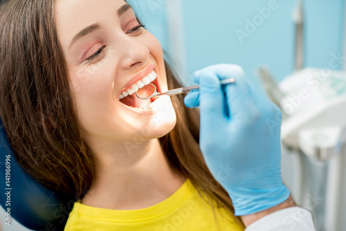 Dentist examining patient teeth with a mouth mirror. Close-up view on the woman's face