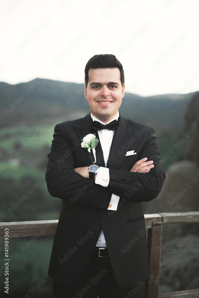 Stylish man, groom posing on the background of mountains Stylish man, groom posing on the background of mountains