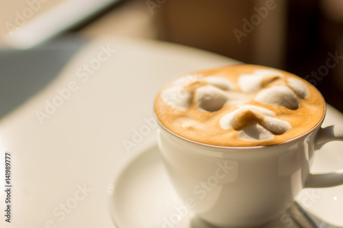 White cup of lattte coffee with sun rise lighting selective focus.