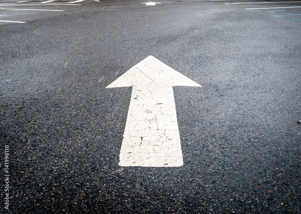 Isolated image of black tar pavement directional white arrow. White street sign arrow pointing up. Street photography during snow storm. Minimal art and design. Abstract street design and traffic sign Isolated image of black tar pavement directional white arrow. White street sign arrow pointing up. Street photography during snow storm. Minimal art and design. Abstract street design and traffic sign