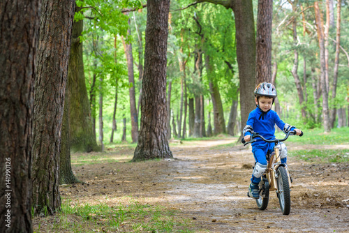 Happy cute blond kid boy having fun his first bike on sunny summer day, outdoors. Happy child making sports. Active leisure for children.Kid boy wear safety helmet. boy is smiling and cicling.
