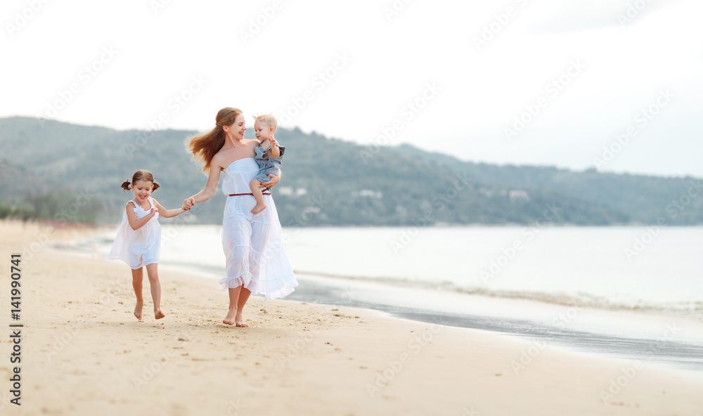 Happy family mother and children on beach by sea in summer