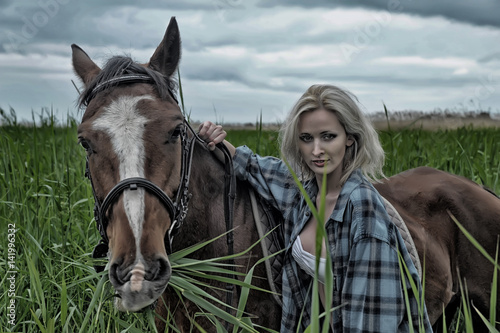 Blonde in a field with a brown horse photo