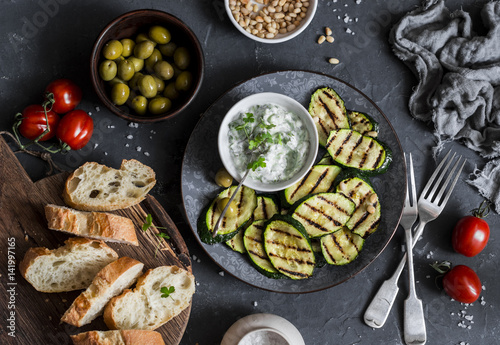 Grilled zucchini, olives, tomatoes, ciabatta - simple snack or appetizer. Mediterranean style food. On a dark background, top view. Flat lay