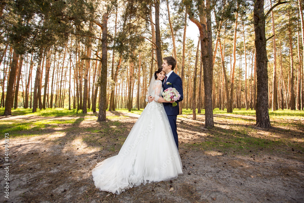 Beautiful wedding couple embracing in forest after wedding ceremony. Bride and groom in love