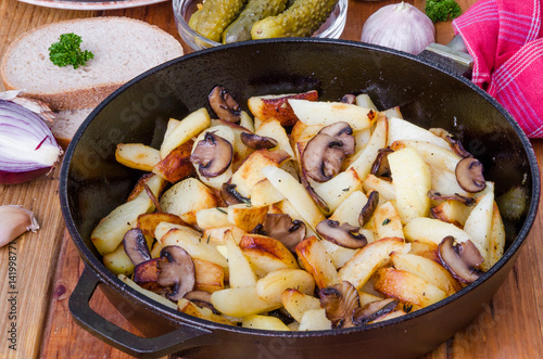 Fried potatoes with mushrooms in a pan on a wooden background