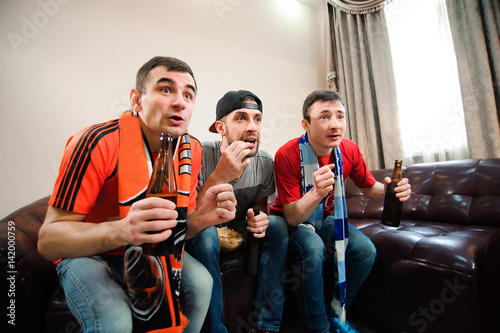 Friends cheering and drinking alcohol while watching soccer match on TV
