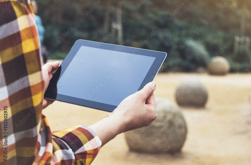 Hipster person holding in hands digital tablet with empty blank screen, computer on background nature park landscape, mock up technology, female hands tourist using gadget