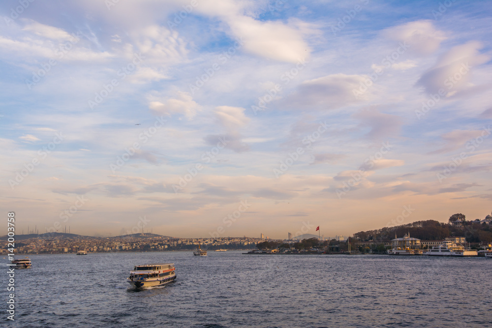 Scenic view with clouds on sunset sky over Bosporus with touristic ships and the city in the background in Istanbul, Turkey