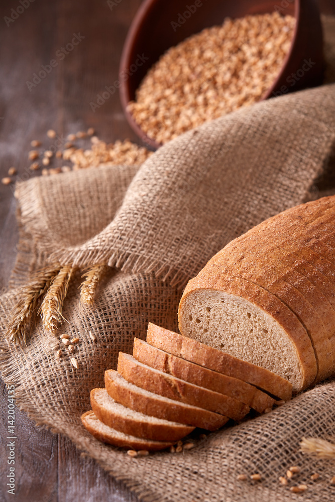 Slices of bread on burlap on the wooden table. composition with wheat ears scattered around and ears of wheat. Slices of bread on burlap on the wooden table. composition with wheat ears scattered around and ears of wheat.