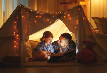 happy family father and child daughter reading a book  in  tent at home.