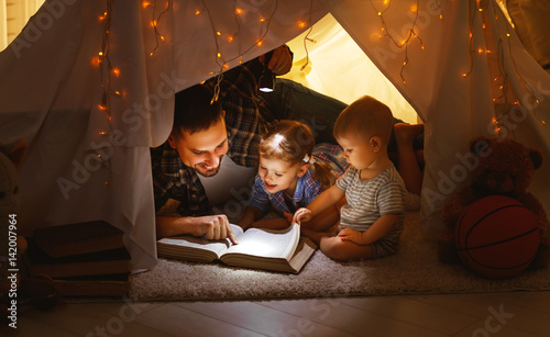 happy family father and children reading a book  in  tent at home.