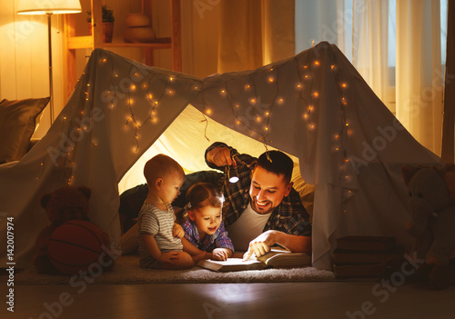 happy family father and children reading a book in tent at home.