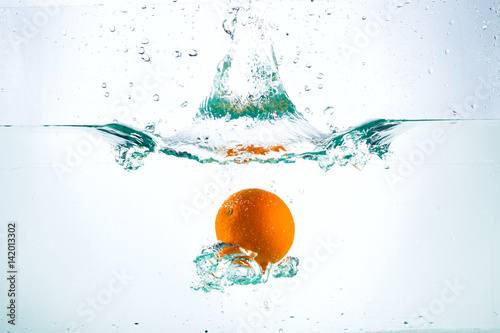 Orange in a stream of water on a white background, studio light