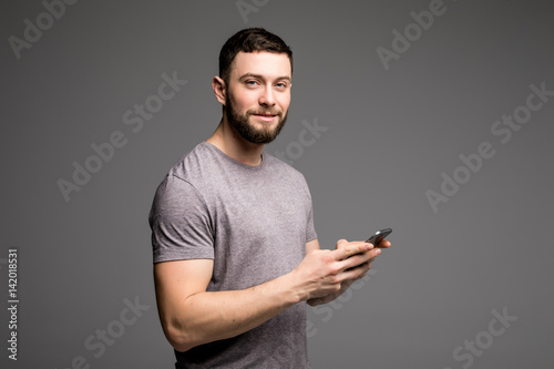 Handsome young man in shirt holding mobile phone and looking at camera while standing against grey background