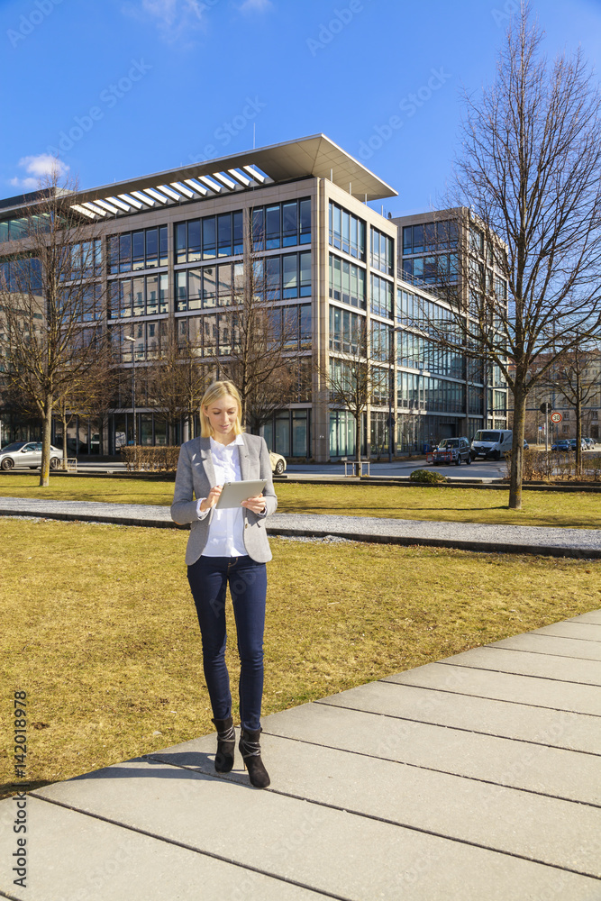 Junge Business-Frau draußen in der Mitagspause mit Tablet in der  Hand, blauer Himmel und Bürogebäuse im Hintergrund