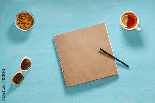 Flat composition of sketch book, pensil, sunglasses and saucer with almonds photo