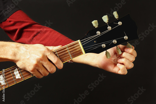 Hands of rock guitarist tunes the guitar on a dark background