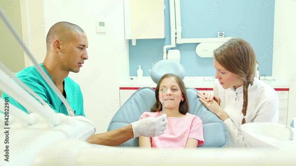 Friendly male dental surgeon and female dentist showing mouth mirror to cute little girl Friendly male dental surgeon and female dentist showing mouth mirror to cute little girl