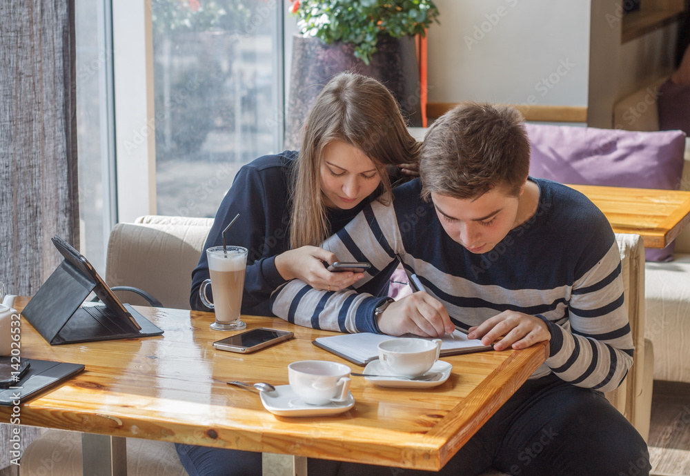 Beautiful young couple  sitting in cozy coffee shop. Couple in love making planning of life and writing in notepad.