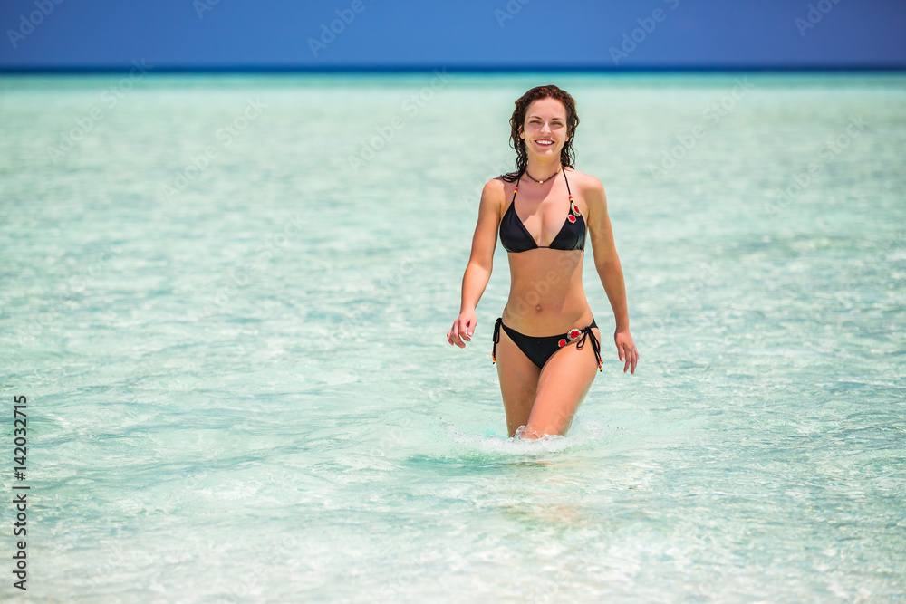 Attractive young woman enjoys Maldivian beach walking in the ocean water