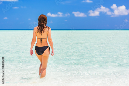 Attractive young woman enjoys Maldivian beach walking in the ocean water
