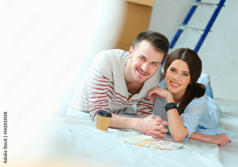 Couple choosing paint colour from swatch for new home lying on wooden floor Couple choosing paint colour from swatch for new home lying on wooden floor