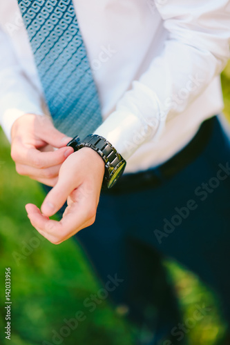 A man in a shirt and tie, puts his hand on the clock. Wedding groom accessories.