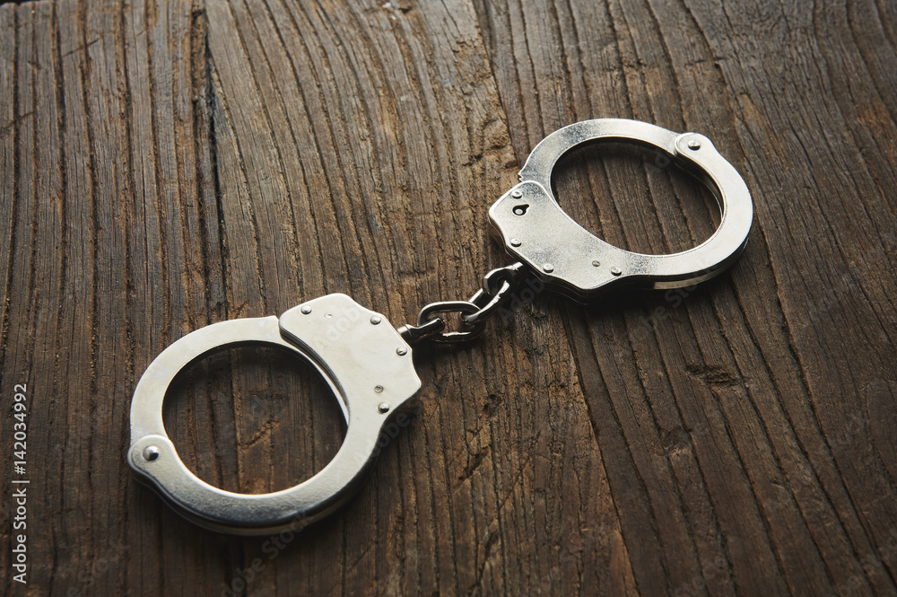 Handcuffs isolated on wooden table Handcuffs isolated on wooden table