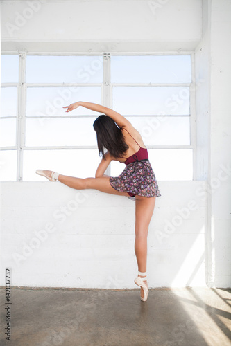 Young dancer woman stretches herself near window photo