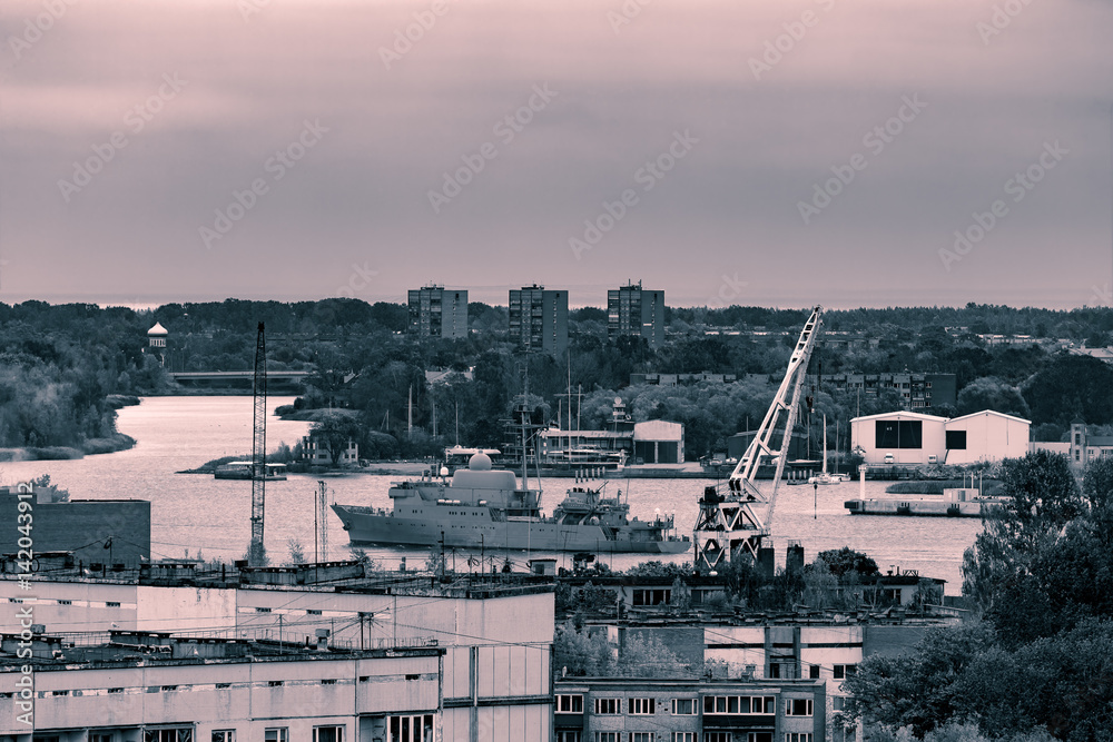 Military ship sailing past the cargo port in Riga, Latvia