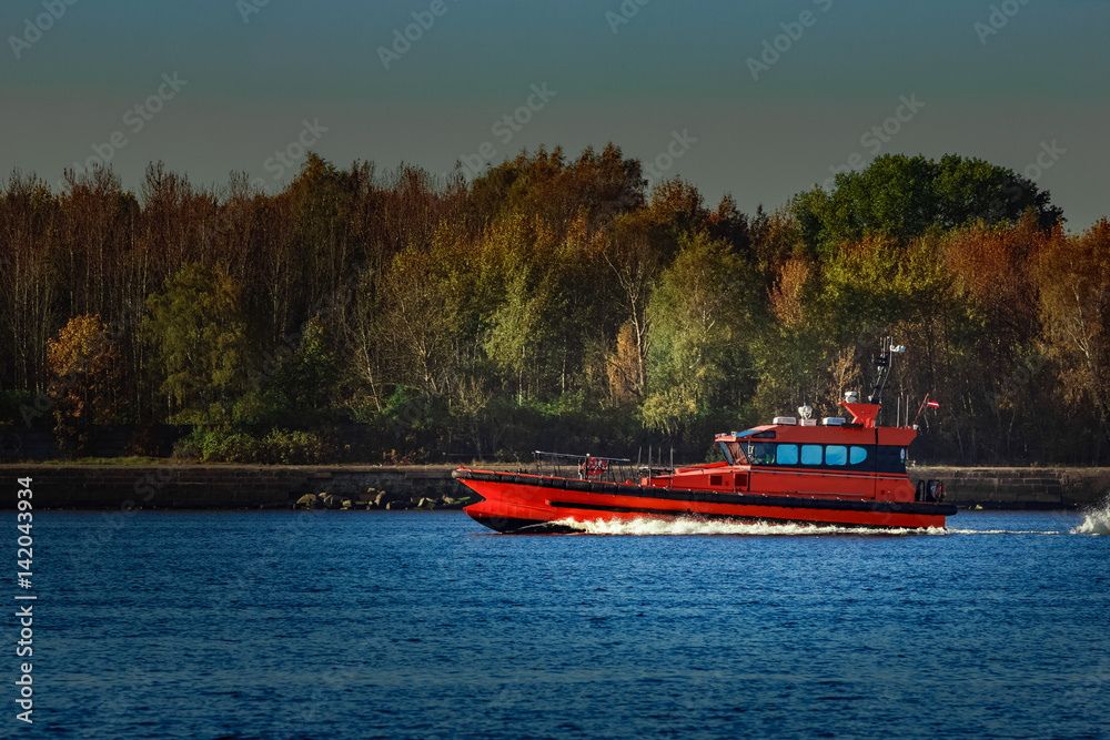 Obraz premium Red pilot ship moving past the autumn trees in Europe