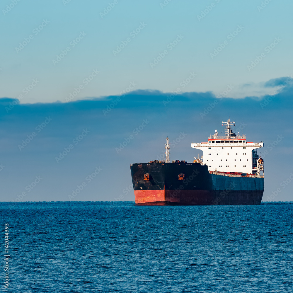 Black cargo ship moving in still Baltic sea water. Riga, Europe Black cargo ship moving in still Baltic sea water. Riga, Europe